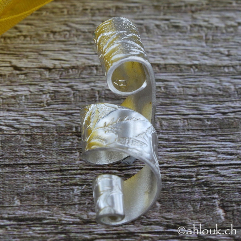 May include: A silver ring with a textured, swirling design. The ring is made of metal and has a unique, organic shape.