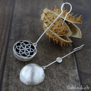 May include: A pair of silver earrings with a geometric design. One earring has a circular design with a cutout pattern, while the other earring is a solid, smooth circle.