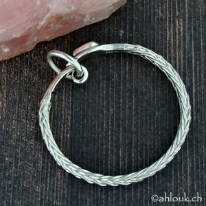May include: Silver key ring with a braided design. The ring is round and has a small loop at the top.