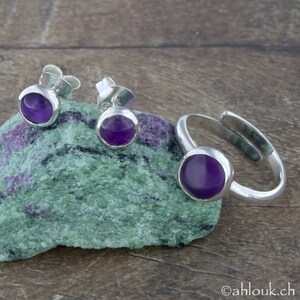 May include: A set of sterling silver jewelry featuring amethyst gemstones. The set includes a ring and a pair of earrings.