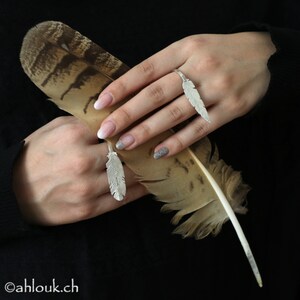 May include: Two silver feather rings on a hand holding a brown and white feather. The rings are designed to fit on the middle and index finger.