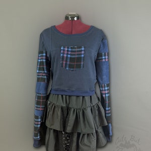 May include: A blue and black plaid long-sleeved shirt with a blue pocket and a black ruffled skirt. The shirt has a cropped length and the skirt has multiple layers.