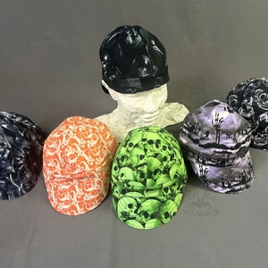 May include: Six different welding caps with skull and skeleton designs. The caps are in various colors, including black, white, orange, green, and purple. The caps are made of a soft, comfortable fabric and are perfect for protecting your head and hair from sparks and heat.