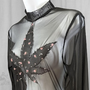 May include: A black sheer long-sleeve mock neck top featuring a large central leaf-shaped appliqué. The appliqué is made of black fabric with a small pink floral pattern and silver sequin accents. The text Cute But Threadly is visible.