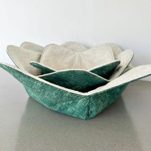 May include: A set of three green and white fabric bowls. The bowls are folded into a flower shape.