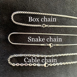 May include: Three different types of stainless steel chains: box chain, snake chain, and cable chain. The chains are laid out on a black surface.