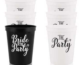 May include: Set of six plastic cups for a bridal party. Four white cups with the text "The Party" and a ring design. Two black cups with the text "Bride of the Party" and a ring design.