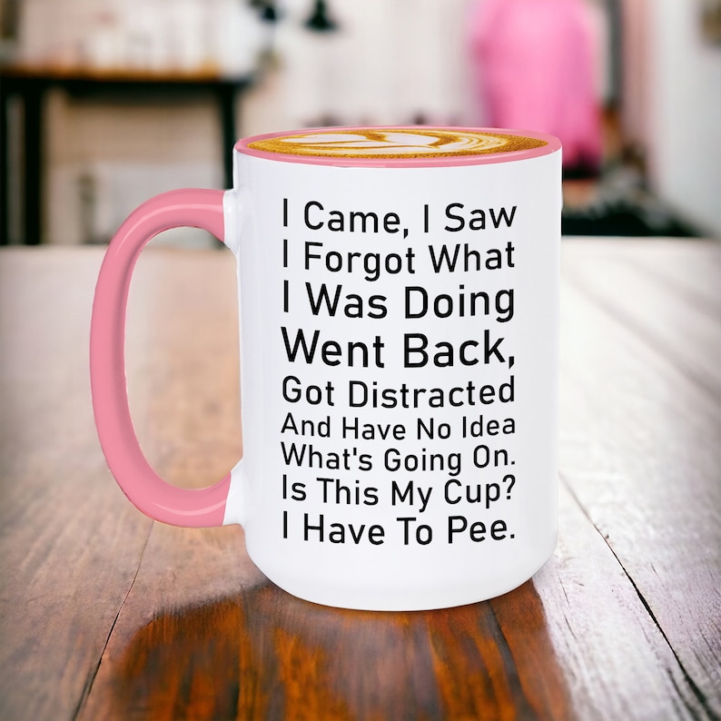 May include: White ceramic coffee mug with a pink rim and handle. The mug has black text that reads: "I Came, I Saw, I Forgot What I Was Doing, Went Back, Got Distracted And Have No Idea What's Going On. Is This My Cup? I Have To Pee."