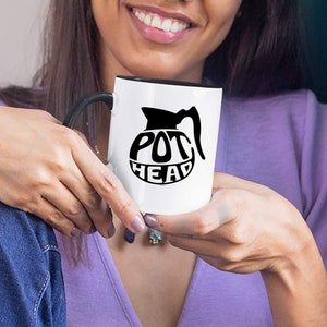 May include: White coffee mug with a black rim and handle. The mug has a black graphic of a coffee pot with the text "POT HEAD" inside the pot.