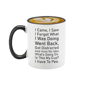 May include: White ceramic coffee mug with a black handle. The mug has a black rim and a humorous saying printed on it: "I Came, I Saw, I Forgot What I Was Doing, Went Back, Got Distracted And Have No Idea What's Going On. Is This My Cup? I Have To Pee."