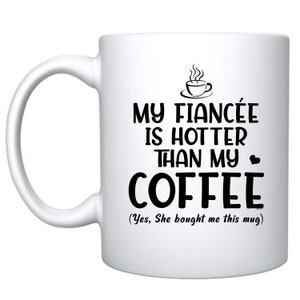 Könnte beinhalten: Eine weiße Keramik-Kaffeetasse mit schwarzem Text, der lautet: "Meine Verlobte ist heißer als mein Kaffee (Ja, sie hat mir diese Tasse gekauft)".