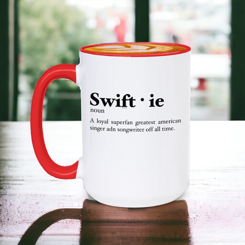 Pu&ograve; includere: Tazza in ceramica bianca con manico e bordo rossi. La tazza presenta la parola "Swiftie" in nero, insieme a una definizione. La definizione recita: "Una superfan leale, la pi&ugrave; grande cantante e cantautrice americana di tutti i tempi."