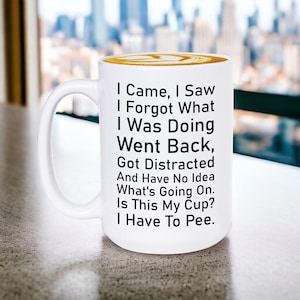 May include: White ceramic coffee mug with black text that reads: "I Came, I Saw, I Forgot What I Was Doing, Went Back, Got Distracted And Have No Idea What's Going On. Is This My Cup? I Have To Pee."