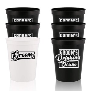 May include: Set of six black and white plastic cups.  Four cups have the text "Groom's" printed on them. One cup has the text "Groom" printed on it. One cup has the text "Groom's Drinking Team" printed on it.