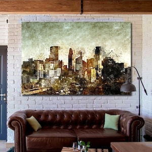 May include: A brown leather sofa with two green throw pillows sits in front of a large canvas print of a city skyline. The print is in shades of brown, gray, and white. The sofa is in a living room with a white brick wall, wooden beams, and a wooden floor.