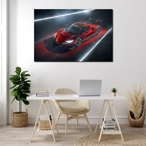 May include: A framed canvas print of a red sports car. The car is angled, showcasing its sleek design and aerodynamic features. The background is dark with bright white and red lighting, highlighting the car's details. The print is displayed above a white desk.