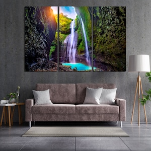 Può includere: Una stampa su tela a tre pannelli che presenta una lussureggiante cascata verde che scende da una scogliera rocciosa. L'acqua è di un blu turchese vibrante e la vegetazione circostante è di un verde intenso. La stampa è perfetta per aggiungere un tocco di natura a qualsiasi stanza.