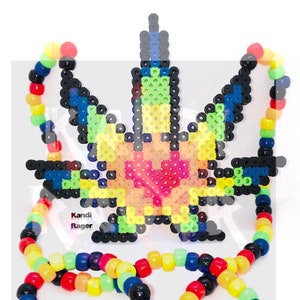 May include: A vibrant beaded necklace and pendant set. The pendant is shaped like a marijuana leaf, with a heart at its core, crafted from an array of beads in shades of black, blue, green, yellow, and pink. The necklace is made of rainbow-colored beads. The image includes the text "Kandi Rager".