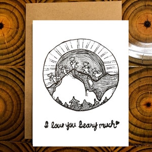 May include: A white greeting card with a black and white illustration of bears on a mountain with a sun in the background. The text "I love you beary much" is written below the illustration. The card is inside a brown envelope.