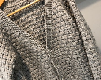 May include: A gray knitted cardigan with a v-neck and button closure. The cardigan has a textured, waffle-like pattern.