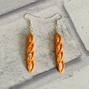 May include: A pair of silver dangle earrings with a brown, twisted bread-shaped charm.