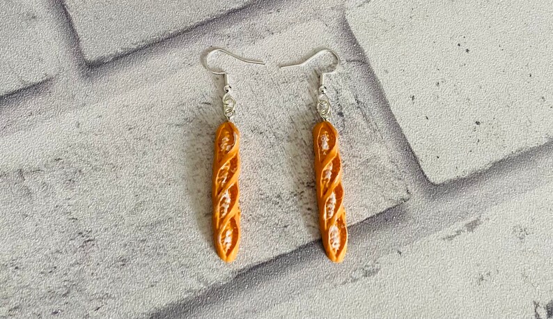 May include: A pair of silver dangle earrings with a brown, twisted bread-shaped charm.