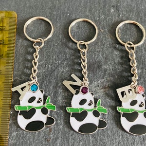May include: Three silver keychains with panda bear charms. Each charm features a different letter, A, N, and B, with a jeweled accent. The charms are attached to a silver chain and a silver key ring.
