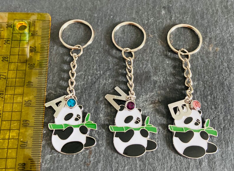 May include: Three silver keychains with panda bear charms. Each charm features a different letter, A, N, and B, with a jeweled accent. The charms are attached to a silver chain and a silver key ring.