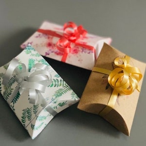 May include: Three gift boxes with different patterns and colors. The boxes are tied with ribbons in silver, gold, and red.