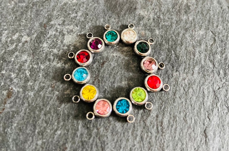 May include: A set of 12 silver-toned charms with colorful crystal accents. Each charm features a small loop for attaching to jewelry or other crafts.