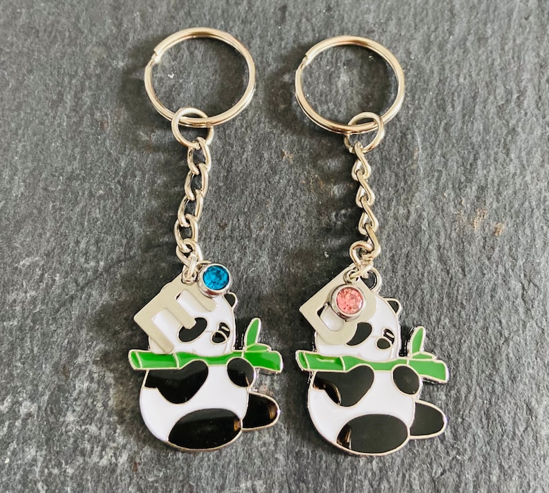 May include: Two silver keychains with panda bear charms. The panda bears are holding bamboo stalks and have blue and pink rhinestones on their heads.