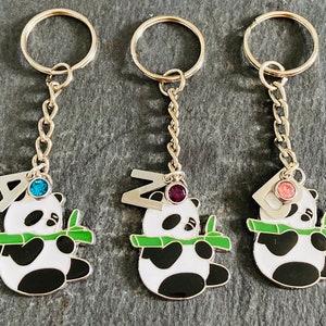 May include: Three silver keychains with panda bear charms. Each panda is holding a green bamboo stalk and has a letter charm above it. The letters are A, Z, and D. Each letter charm has a different colored rhinestone: blue, purple, and pink.