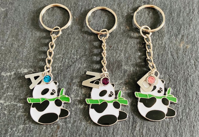 May include: Three silver keychains with panda bear charms. Each panda is holding a green bamboo stalk and has a letter charm above it. The letters are A, Z, and D. Each letter charm has a different colored rhinestone: blue, purple, and pink.