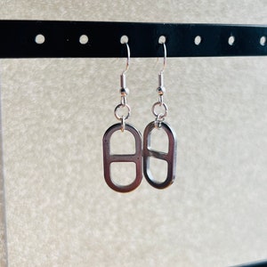 May include: A pair of silver earrings with a unique design. Each earring features a silver oval shape with a smaller oval cut out in the centre.