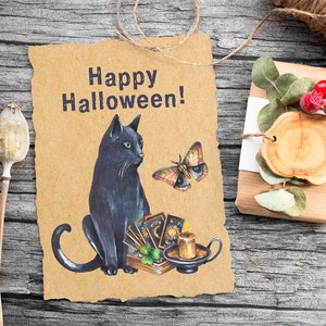 Pu&ograve; includere: Un biglietto marrone con il testo "Happy Halloween!" e un gatto nero seduto accanto a una candela e carte dei tarocchi. Una farfalla vola sopra il gatto.