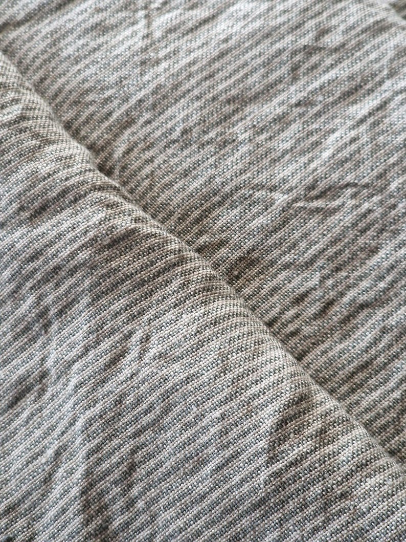 May include: A piece of fabric featuring a heathered gray and white color palette with a visible woven texture. The material displays a subtle cross-hatch pattern created by the interlacing of light and dark threads, resulting in a soft, mottled appearance across the surface of the textile.