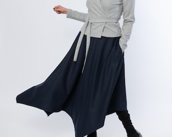 May include: A light gray wrap jacket with a matching belt and a long, flowing navy blue skirt. The skirt has a unique asymmetrical hemline. The outfit is paired with black shoes and black leg warmers.