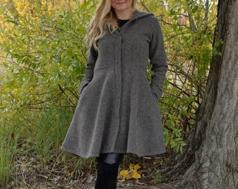 May include: A charcoal gray hooded coat featuring a fitted bodice, a flared skirt, long sleeves, and a front button closure. The coat is paired with black leggings and black knee-high boots, creating a cohesive look for cooler weather conditions.