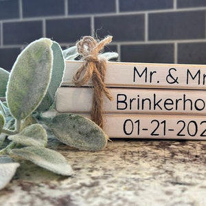 May include: A stack of three wooden blocks with the text "Mr. & Mrs. Brinkerhoff 01-21-2023" written in black. The blocks are tied together with twine.