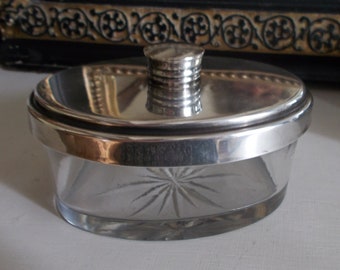 May include: A silver-plated oval-shaped glass jar with a star-shaped design on the bottom and a silver lid with a knob on top.