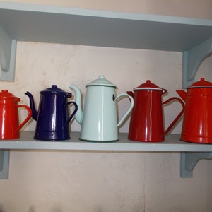 Può includere: Cinque caffettiere smaltate su uno scaffale. Le caffettiere sono rosse, blu e blu chiaro. Sono tutte nello stesso stile con un manico da un lato e un beccuccio dall'altro.
