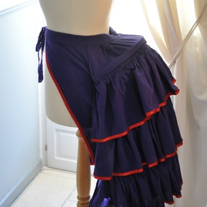 May include: A purple and red ruffled skirt with a red ribbon trim. The skirt is on a white dress form.