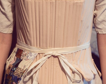 May include: A white cotton corset with a white ribbon tied at the waist. The corset has a quilted design and is worn over a white shirt. The text "Couture Madame Laurena Victorian" and "Sandrine Delatte photographe" is visible at the bottom of the image.