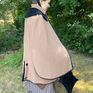 May include: A brown cape with a black velvet collar and black trim. The cape is worn over a striped skirt and a black umbrella is held in the right hand.