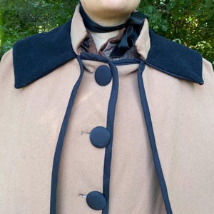 May include: A tan wool cape with a black velvet collar and black trim. The cape has four black buttons down the front.