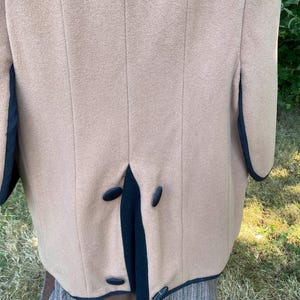 May include: A tan wool coat with black trim and four black buttons down the back.