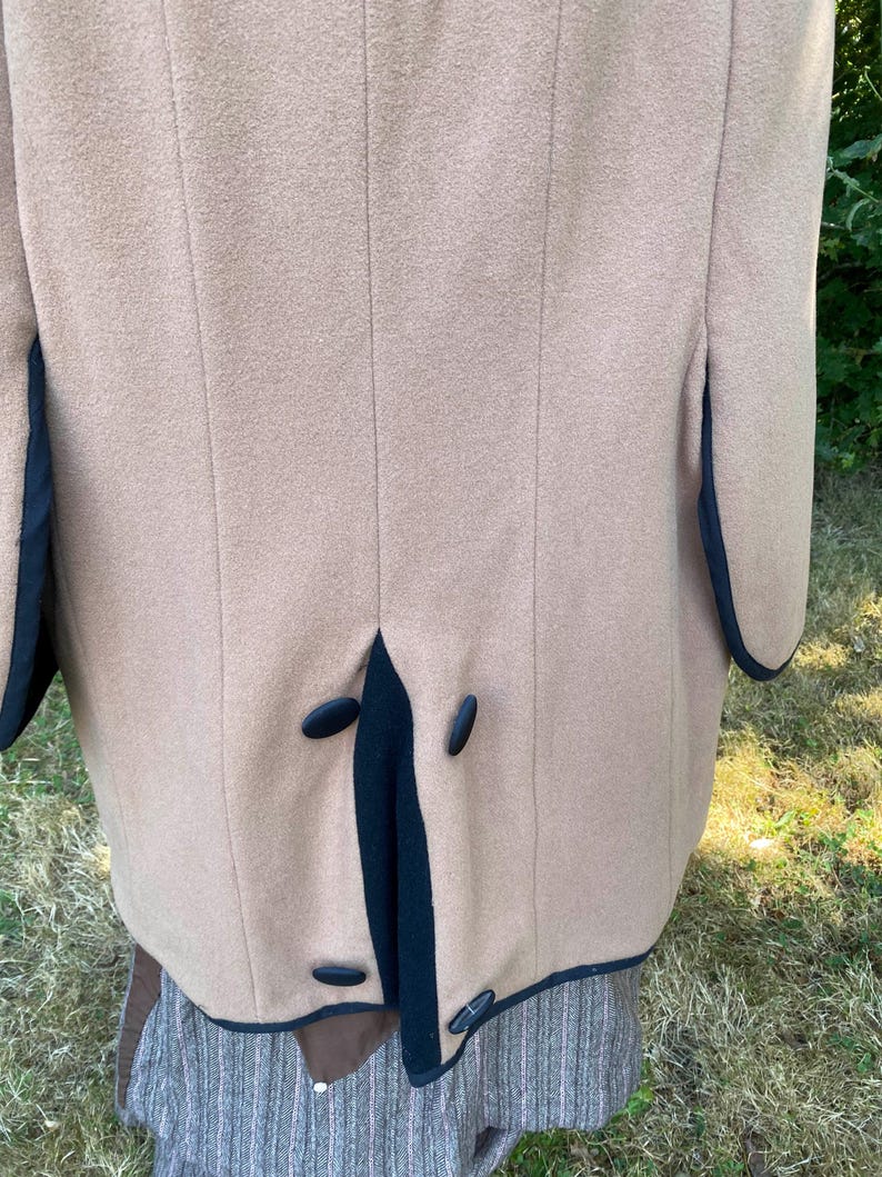 May include: A tan wool coat with black trim and four black buttons down the back.