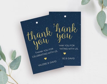 Peut inclure: Deux étiquettes de remerciement bleu marine avec des lettres dorées. Le texte sur les étiquettes est "merci" et "Merci d'avoir célébré avec nous. Valerie & David" et "Merci de nous avoir évalués. Rie & David".
