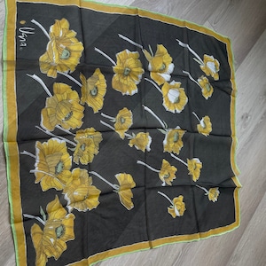 Peut inclure: Un foulard en soie noir avec un motif floral jaune. Le foulard a une bordure verte et dorée et le mot "Uma" est imprimé dans le coin supérieur gauche.