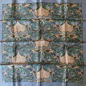 May include: A square silk scarf featuring a repeating floral pattern with stylized green leaves, golden-brown flower petals, and blue centers against a muted grey background. The design includes intricate line work and a solid grey border.